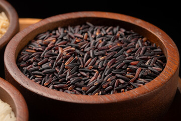 Purple Riceberry rice grains in a brown wooden bowl on black background