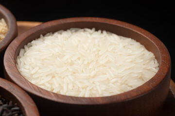Jasmine rice grains in a brown wooden bowl on black background