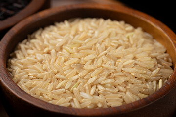 Brown rice grains in a brown wooden bowl. Close-up
