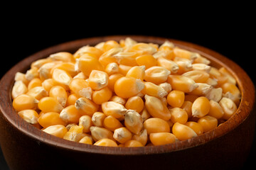 Close-up of raw corn kernels in a brown wooden bowl on black background