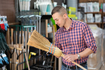 Male buyer carefully chooses broom in hardware store to clean the yard of her house