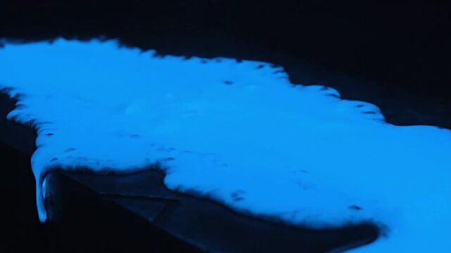 Mesmerizing radiant blue fluid illuminated against a dark background, depicting an an abstract, scientific phenomenon or futuristic chemical reaction