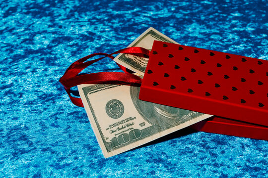 Red gift box with fake dollar notes on blue velvet surface