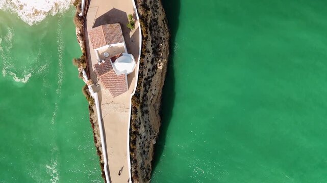 Top-Down Aerial Perspective of the White Church of Nossa Senhora da Rocha Perched on a Narrow Limestone Cliff Above the Atlantic Ocean in the Algarve Region of Portugal
