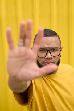 Man in yellow shirt making stop gesture in front of yellow background