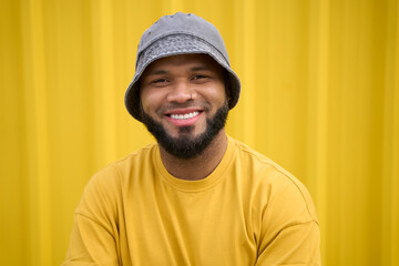 Smiling man in bucket hat and yellow shirt against yellow background