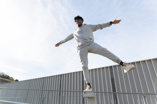Man in grey tracksuit balancing on railing with open arms