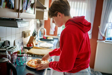 Teenager boy baking pizza at home in oven.