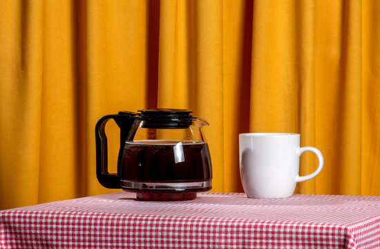 Coffee pot and mug on checkered tablecloth with yellow background