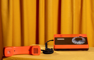 Retro orange rotary phone and handset on yellow table with curtain