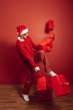 Santa hat wearing adult kicking Christmas gift boxes in red festive room