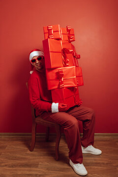 Santa hat man balancing red gift tower indoors at Christmas