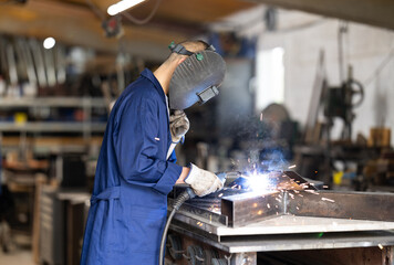 Male welder standing with a welding semi-automatic machine and a safety helmet in a metal machining workshop