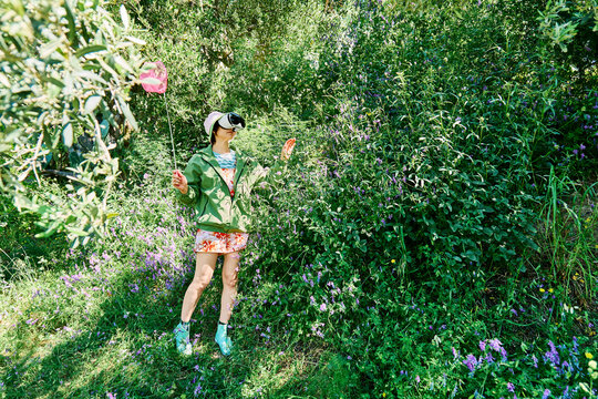 Woman with virtual reality glasses and butterfly net in a blooming meadow