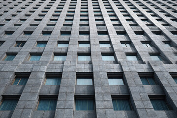 Modern corporate skyscraper facade with evenly spaced rectangular windows and gray stone texture, creating repetitive pattern that emphasizes height and architectural design