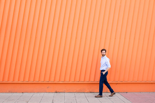 Business man walking by orange wall outdoors with copy space