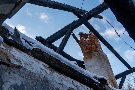 View from inside abandoned house in winter shows charred roof structure damaged chimney and open sky above