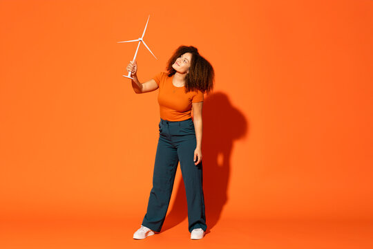 Woman looking at wind turbine model in font of orange background