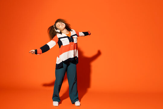Woman standing in front of orange background with wireless headphones