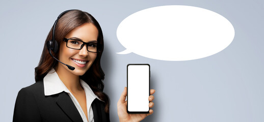 Customer support callcenter phone operator in glasses, headset hold show point smartphone cell phone mobile blank mockup screen, isolated gray grey background. Call center. Empty mock up speech bubble