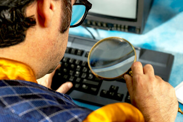 Businessman using magnifying glass to examine keyboard at office desk