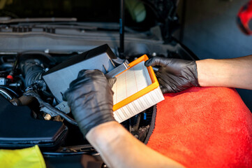 Technician changing the air filter in a car engine compartment, ensuring optimal performance and cleanliness of the vehicle air intake system. High quality photo