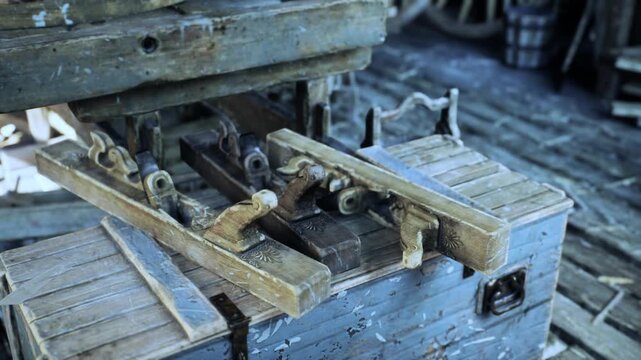 An old carpentry workshop showcases various vintage tools, highlighting the craftsmanship of earlier times. The rustic setting features wooden surfaces and worn equipment that reflect a rich history.