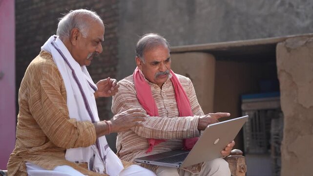 two indian senior farmers using laptop 