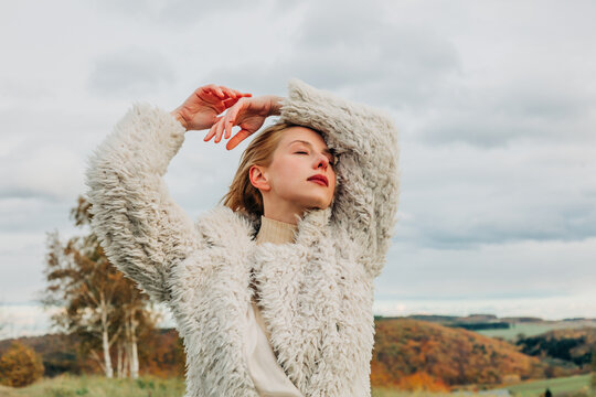 Fashionable person in white sheep wool jacket posing outdoors in autumn