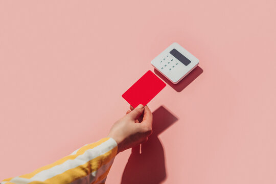 Hand in yellow shirt paying contactless by card on pink background