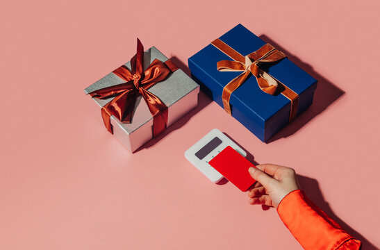 Contactless payment with credit card and gift boxes on pink background