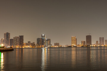 Fototapeta premium Sharjah, UAE,10.10.2025. City skyline at night with water reflections and bright lights in the urban area.