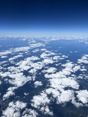 飛行機の上空から撮影した広大な雲海と青空の風景 どこまでも続く水平線と白い雲が織りなす空の旅のイメージ 旅行やビジネスの移動を感じさせる航空写真 爽やかなブルーとホワイトのコントラストが美しい大気のバックグラウンド
