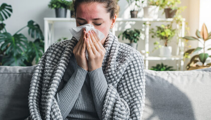 Generated image. Woman sitting on couch with tissue in hand, feeling unwell and wrapped in blanket in living room with plants