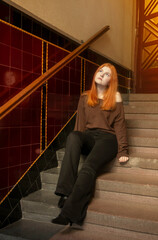 A young beautiful woman sits on the stairs in the entrance of an old house