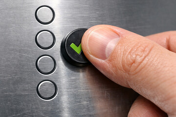 Finger pressing a button with a green checkmark on a metallic surface