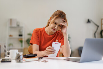 Obraz premium Stressed over bills. Asian woman with laptop holding tax papers alculating dealing financial budget on desk, female worried have stress headache after calculate cost, money problem 