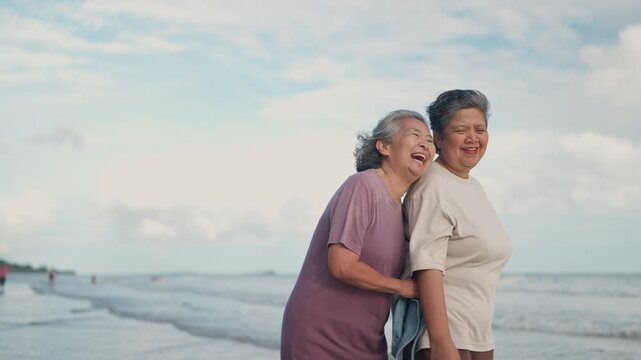 Asian mature LGBTQ couple walking together on a sunny beach by the sea during a romantic vacation