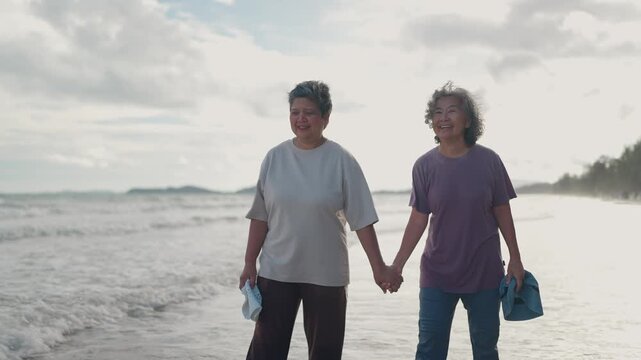 Asian mature LGBTQ couple walking together on a sunny beach by the sea during a romantic vacation