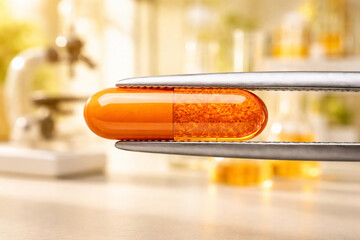 Orange capsule held by tweezers in laboratory