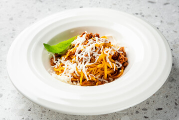 spaghetti Bolognese with rich meat sauce, grated Parmesan cheese, and a fresh basil leaf, served in...