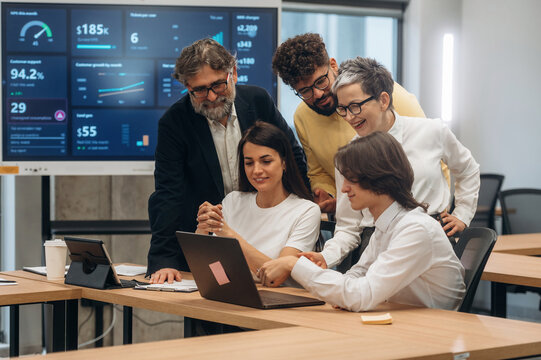 Group of diverse business professionals collaborating in modern office, analyzing data on laptop and discussing strategies for project success and teamwork - Powered by Adobe