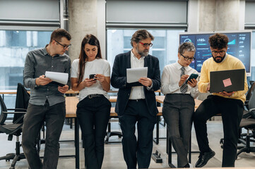 Group of diverse business professionals collaborating in modern office environment, engaged with digital devices, showcasing teamwork and innovation in a corporate setting