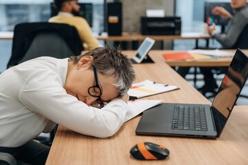 Businesswoman resting her head on desk in modern office environment, showcasing fatigue and the challenges of a busy work life with copy space