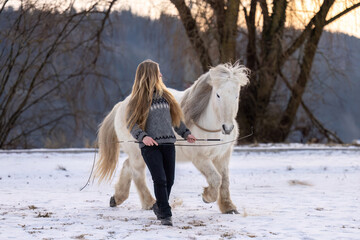 Woman practicing natural horsemanship and free work with a white horse outdoors on a snowy winter field