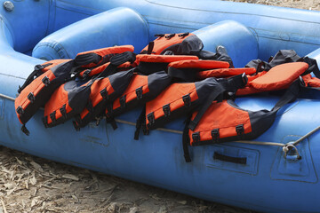 Stack of orange safety life jacket piled inside blue rubber raft waiting for adventure trip river rafting activity representing prepared and organized emotion