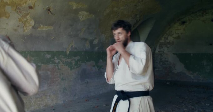 Two male karate practitioners perform circular warm-up movements.