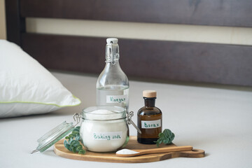 Baking soda, vinegar, and borax, salt are placed on a wooden tray. The scene shows a tidy indoor space with natural light. Sustainable, non-toxic home care solution for fresh and hygienic bedding.