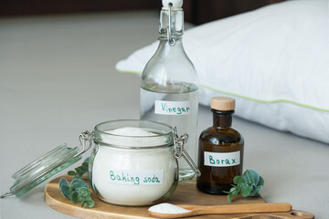 Baking soda, vinegar, and borax, salt are placed on a wooden tray. The scene shows a tidy indoor space with natural light. Sustainable, non-toxic home care solution for fresh and hygienic bedding.