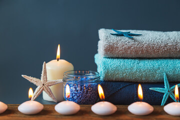 Stack of colored towels, salt, burning candles in a row, shell and starfish.